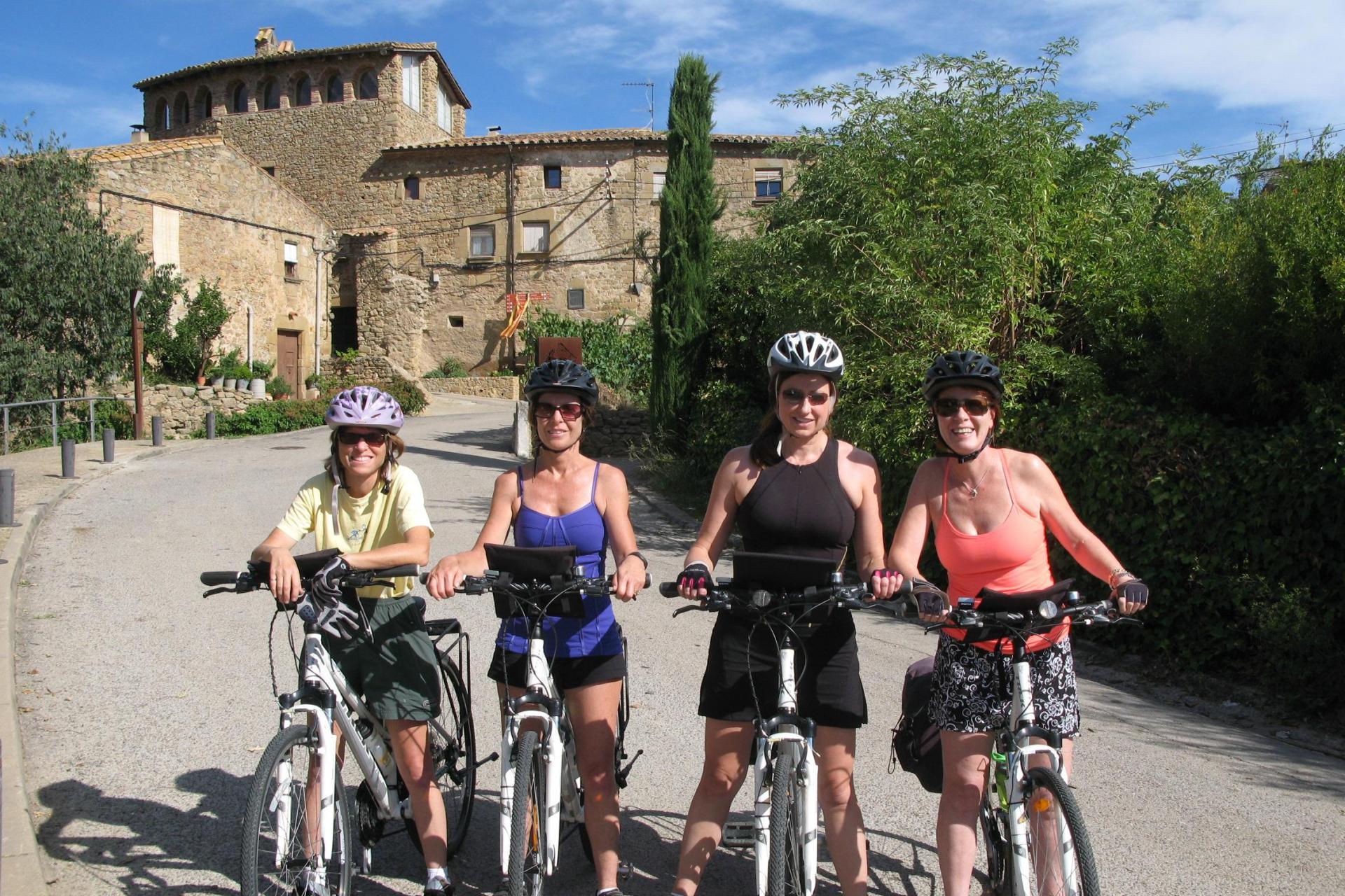 A group of cyclists on a tour stand in the foreground with medieval Spanish architecture in the background
