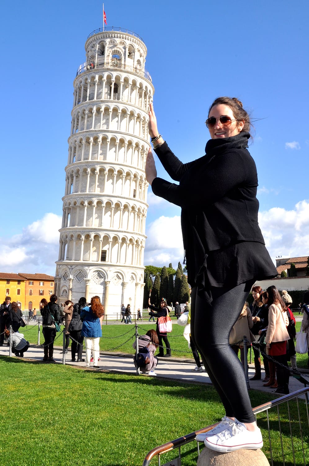 A woman holds her hands to create an optical illusion of holding up the Leaning Tower of Pisa